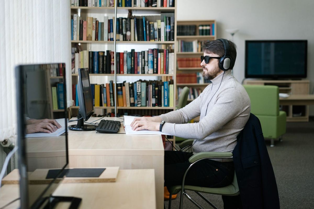 Un homme non-voyant, lunettes noires, travaille sur un ordinateur dans une bibliothèque
